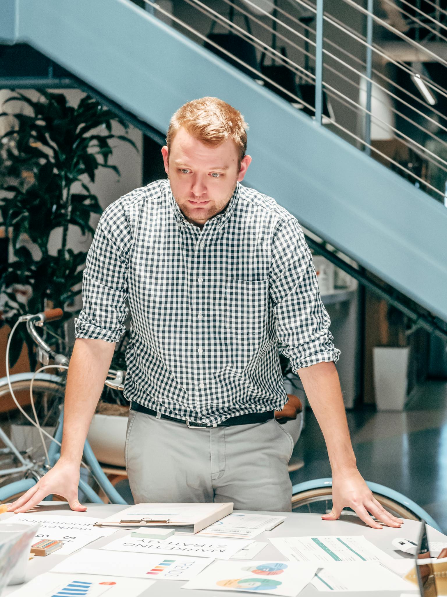 A businessman in a modern office analyzing reports on a table, showcasing teamwork and innovation.